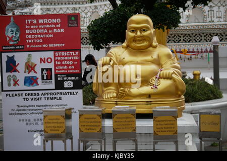 Un Laughing Buddha statue en or est situé en face de Wat Arun et à côté d'une bannière officielle interdisant l'utilisation de bouddha comme un tatouage ou de décoration design. Banque D'Images