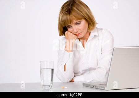 Femme avec verre d'eau, pilules et ordinateur portable Banque D'Images