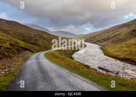 Route sinueuse avec rivière et ciel nuageux dans les montagnes de Glen COE en Écosse, Royaume-Uni Banque D'Images