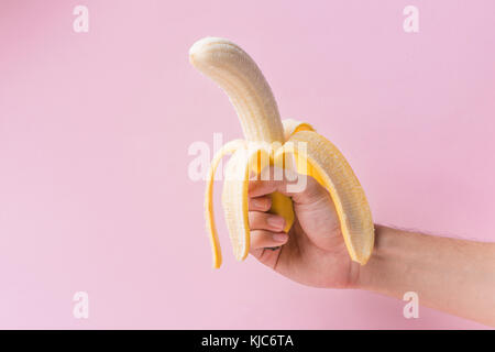 Mains peeling banana isolé sur fond rose. Banque D'Images