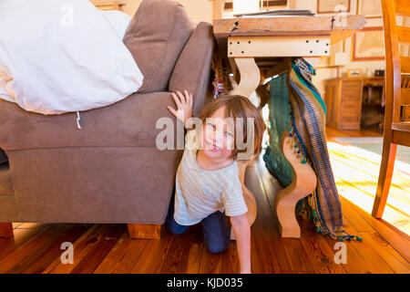 Young boy ramper sur le plancher entre table et canapé Banque D'Images