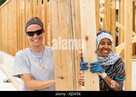 Bénévoles souriants holding lumber at construction site Banque D'Images