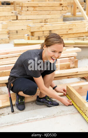 Smiling Caucasian woman measuring lumber at construction site Banque D'Images