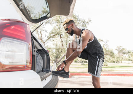 Black man leaning on voiture bicorps attacher ses chaussures Banque D'Images