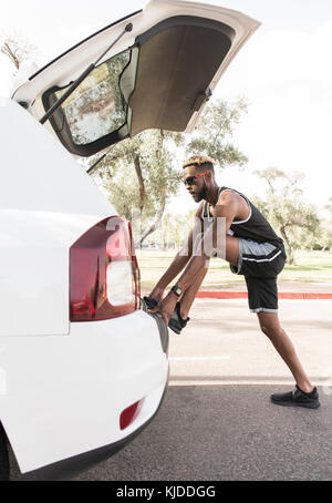 Black man leaning on voiture bicorps stretching leg Banque D'Images