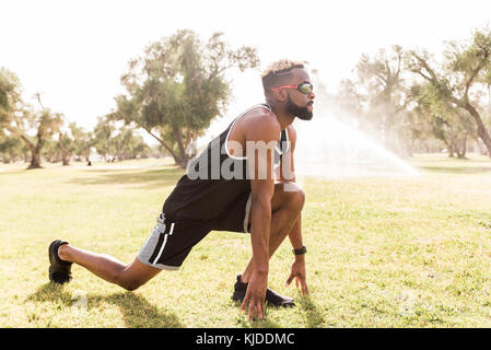 Black man crouching in park qui s'étend les jambes Banque D'Images