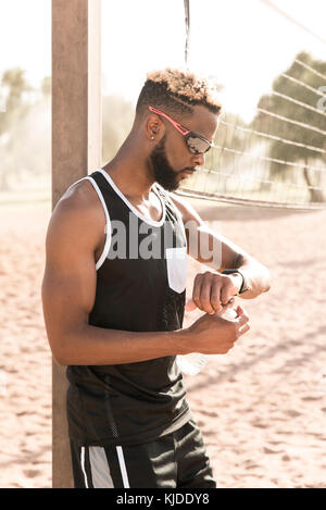 Black man leaning on beach volley-ball net contrôle du temps Banque D'Images