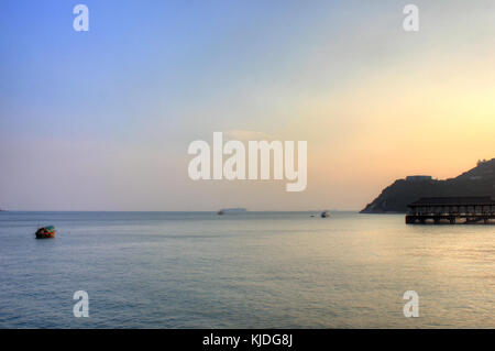 Cette photographie capture le port de Hong Kong au crépuscule, mettant en valeur l'activité portuaire animée, les bateaux et les gratte-ciel imposants de la ville. La lumière qui s'estompe souligne la nature dynamique du port, un centre économique et commercial clé en Asie. Banque D'Images