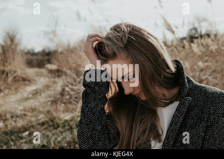 De la beauté et de la mode femme ajustant ses cheveux. Fille européenne debout sur fond de scirpe. Femme s'accrocher à la tête et regardant vers le bas. Gros plan large Banque D'Images