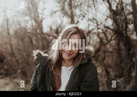 Jolie femme en veste chaude avec de la fourrure à l'extérieur de l'appareil photo. posint Jeune fille européenne avec de longs cheveux blonds, de larges sourcils looking at camera et souriant. Banque D'Images