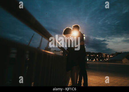 Caucasian couple kissing près de rambarde de nuit Banque D'Images