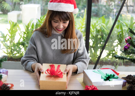 Portrait of asian woman wear santa claus hat à la maison. Girl with gift box actuelle. Noël, nouvel an vacances. joyeux noël accueil saison des fêtes. Banque D'Images