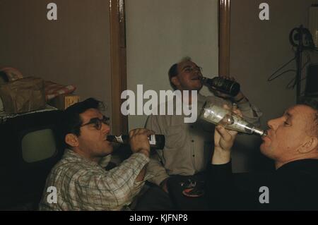 Une photographie de trois hommes posant en buvant des bouteilles de bière, ils sont assis autour d'une petite table où un cigare peut être vu se reposer dans un cendrier, il y a une petite télévision antique en arrière-plan avec des objets empilés dessus, 1952. Banque D'Images