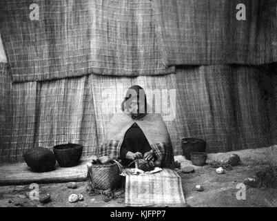 Photographie, imprimée en platine, d'une femme amérindienne, assise au sol, tissage d'un panier, par Edward S Curtis, 1899. De la bibliothèque publique de New York. Banque D'Images