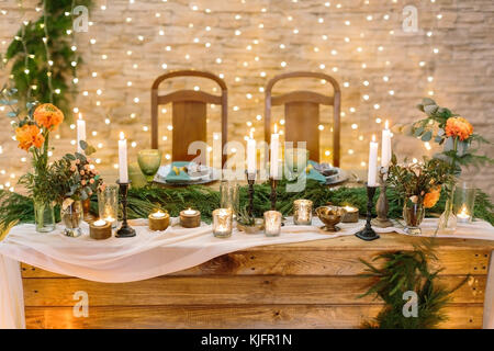 Romance, confort, vacances concept. table romantique pour deux amoureux avec de nombreux des bougies dans divers supports de bougie, elle aussi décorée avec peu de grappes et des lumières sur l'arrière-plan Banque D'Images
