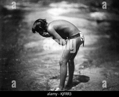 Portrait photographique d'un Apache qui porte de l'eau sur son visage, il a été photographié se nettoyant dans la rivière le matin, il portait seulement un drap de breechCloth comme il se tient au bord de l'eau courante, 1906. De la bibliothèque publique de New York. Banque D'Images