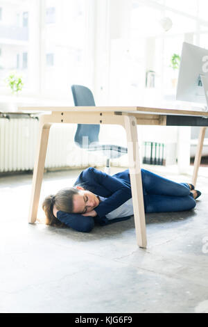 Businesswoman couché sous la table dans office sleeping Banque D'Images