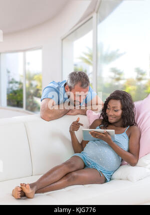 Les futurs parents looking at tablet pc sur le canapé dans la salle de séjour Banque D'Images