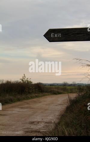 Enseigne de sortie en bois au crépuscule pointant vers la gauche avec chemin de terre allant dans la distance Banque D'Images