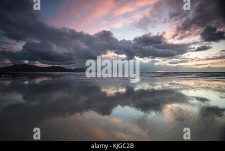 Couchant lumineux et coloré sur une plage du nord du Pays de Galles. La plage de sable mouillé reflète le ciel coloré. Banque D'Images