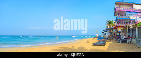 Hikkaduwa, Sri Lanka - 6 décembre 2016 : panorama de l'agréable plage de sable fin de station touristique populaire avec rangée de bars et restaurants de poissons, offrant un tas Banque D'Images