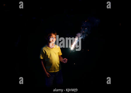 Garçon debout à l'extérieur tenant un sparkler Banque D'Images