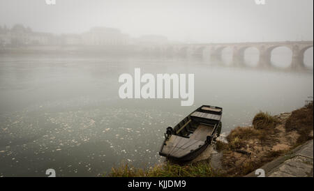 Bateau de pêche "toue" ancré sur les bords de Loire en face d'une vue sur la ville de Saumur brumeux, avec pont Banque D'Images