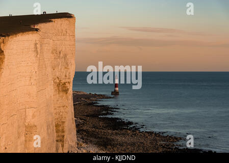 Dangereusement l'homme assis sur le bord de la falaise de Beachy Head au coucher du soleil Banque D'Images