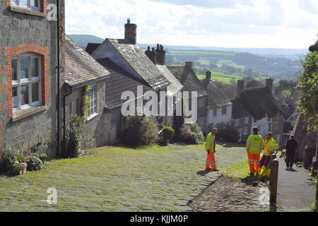 Trois ouvriers discutant de dégager l'herbe des pavés de Shaftesbury Gold Hill, Dorset, Angleterre Banque D'Images