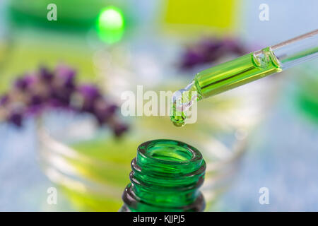 Les bouteilles en verre vert avec des gouttes de liquide essentielle de lavande compte-gouttes sur fond de bois avec des fleurs médicinales Banque D'Images