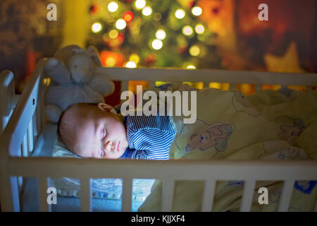 Adorable bébé nouveau-né garçon, dormant dans un lit bébé dans la nuit. Petit garçon au pyjama rayé bleu faire la sieste dans une pièce sombre, la décoration de Noël dans la chambre, Banque D'Images