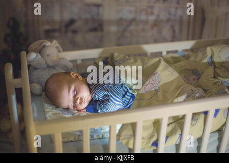 Adorable bébé nouveau-né garçon, dormant dans un lit bébé dans la nuit. Petit garçon au pyjama rayé bleu faire la sieste dans une pièce sombre, la décoration de Noël dans la chambre, Banque D'Images