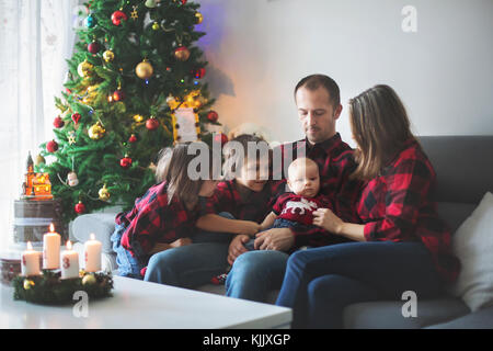 Portrait de famille heureuse à Noël, la mère, le père et ses trois enfants assis sur la table à la maison, décoration chritmas autour d'eux