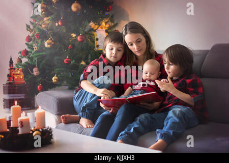 Portrait de famille heureuse à Noël, mère, lire un livre à ses trois enfants assis sur la table à la maison, décoration chritmas autour d'eux