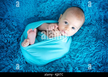 Cute 3 mois bébé garçon en bleu wrap, allongé sur une couverture bleue, à la caméra à curieusement Banque D'Images