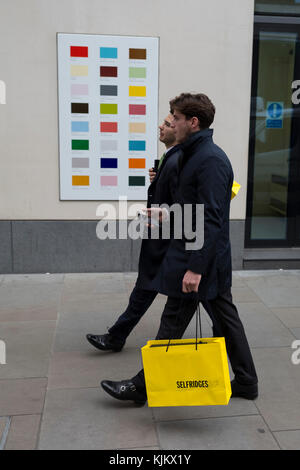 Shoppers portant un sac jaune du grand magasin Selfridges passe devant un échantillon de couleur sur le mur d'une entreprise du centre de Londres, le 22 novembre 2017, à Londres en Angleterre. Banque D'Images