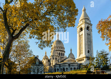 Les trois-quarts arrière vue sur la Basilique du Sacré-Cœur de Paris au lever du soleil en automne avec le clocher carré et les branches d'arbres en premier plan Banque D'Images