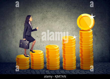 Businesswoman with briefcase intensifier une échelle escalier financière faite de pièces d'or Banque D'Images