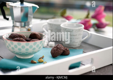 De cacao et de pistaches biscuits rustiques sur plateau en bois avec cafetière, tasses, des pistaches, des morceaux de sucre et des fleurs dans l'arrière-plan Banque D'Images