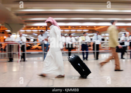 Les hommes et les amis greeters en attente dans la zone des arrivées du Terminal1 greeters et un passager en vêtements arabes avec un wheelie-bag walking passé, le motion blur Banque D'Images