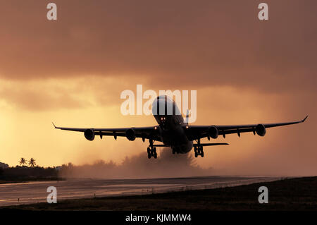 Airbus A340-313X décollage au crépuscule d'une piste mouillée des pluies avec l'échappement du moteur faire une pulvérisation d'eau Banque D'Images