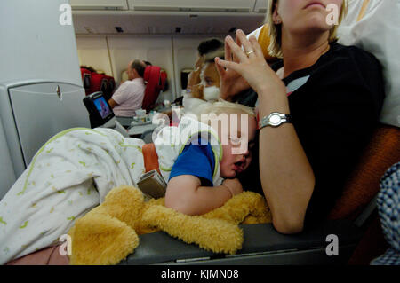 Un jeune enfant endormi sur les genoux d'une femme dans la cabine de classe économique d'un Boeing 747-400 de Virgin Atlantic en route. Banque D'Images