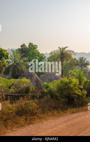 Huttes de chaume traditionnel tour de Guinée Bissau cachée parmi les arbres et palmiers de gravier pendant le coucher du soleil, l'Afrique de l'Ouest Banque D'Images