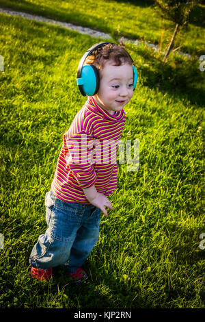 Adorable bambin mumbles et se déplace à l'air dans le casque tout en jouant sur une pelouse au coucher du soleil Banque D'Images