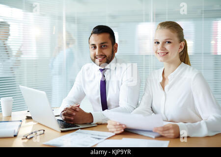 Jeune homme et femme en vêtements de forme regardant la caméra tout en travaillant Banque D'Images