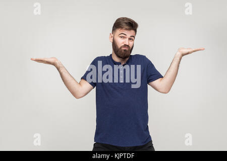 Homme barbu émotif pas sûr pour quelque chose. Studio shot, fond gris Banque D'Images