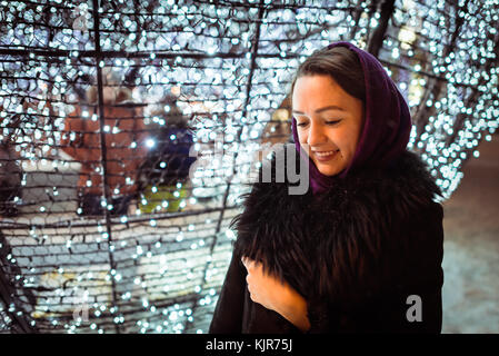 Jeune femme dans des vêtements chauds d'un séjour près de décorations de Noël à la recherche vers le bas et souriant Banque D'Images