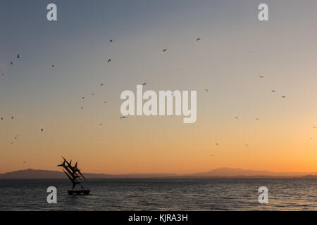 Flock of birds flying over une sculpture sur Passignano (Lac Trasimène) au coucher du soleil Banque D'Images