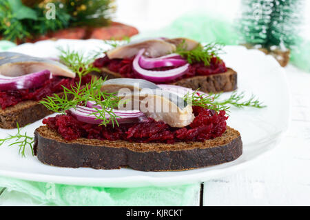 Les sandwiches avec du hareng, des betteraves, l'oignon rouge sur le pain de seigle sur un fond de bois blanc. Banque D'Images