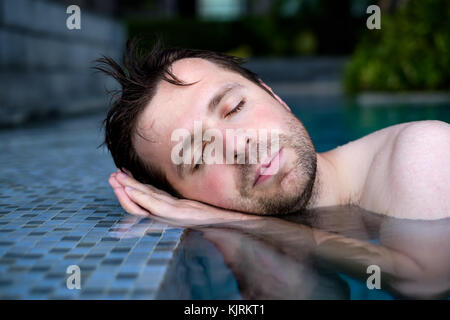 Un jeune homme prétend qu'il est en train de dormir sur le bord de la piscine, mettant ses mains sous sa tête. Banque D'Images